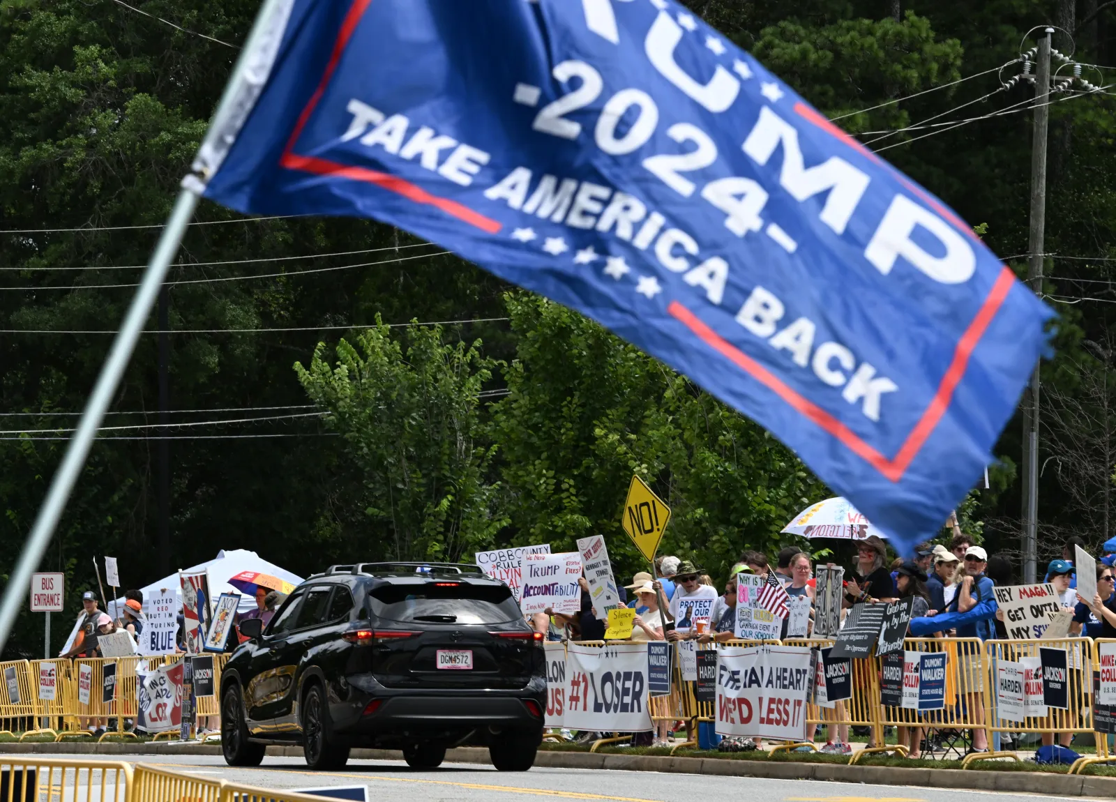 Protesters opposed to President Donald Trump's visit hold signs as he arrives outside Wheeler High School on July 22 in Marietta, Georgia.