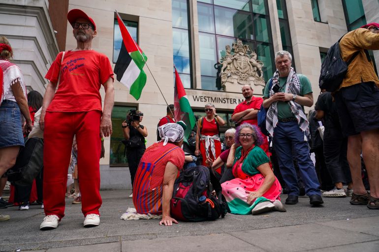 Demonstrators sit outside the Westminster Magistrates Court in London on Thursday as a plea hearing for 25 people accused of showing support for Palestine Action takes place