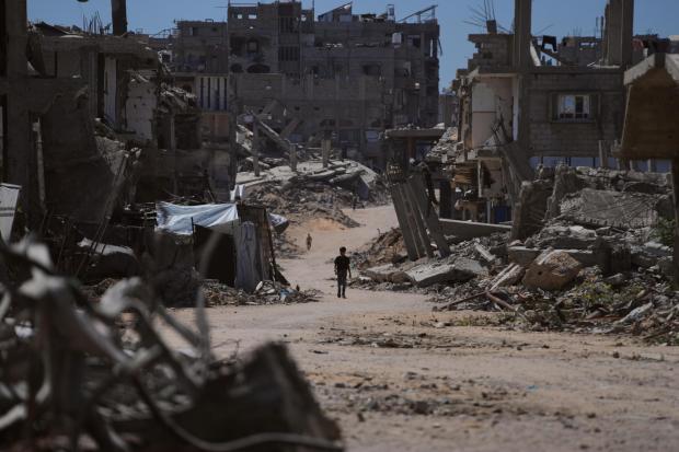 A Palestinian child walks along a street surrounded by buildings destroyed in Israeli military strikes.