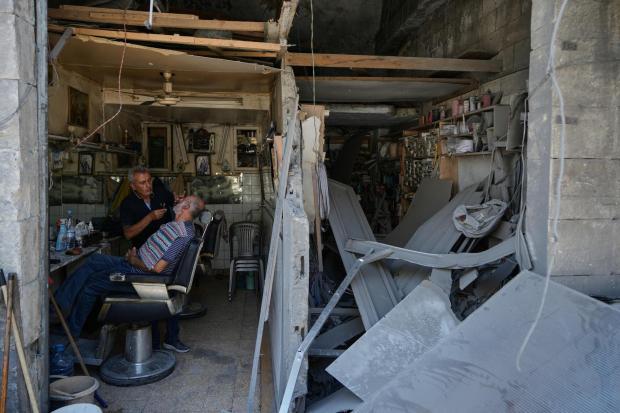 Barber Ali Sbouri grooms a client's beard inside his shop damaged in Israeli airstrikes.