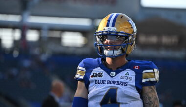 A football player wearing a Blue Bombers uniform and helmet stands on the field during a game.