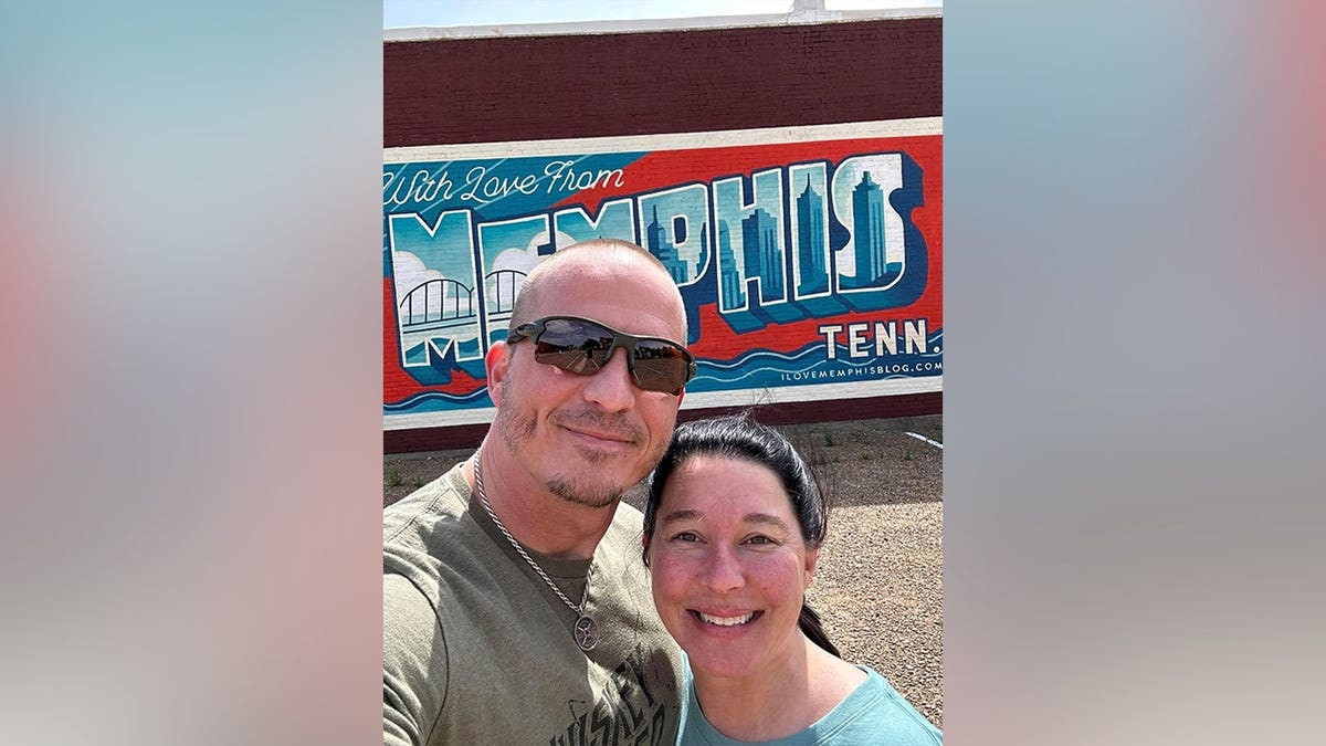 Justin Elrod and Lena Elrod smile for a selfie in front of a colorful 