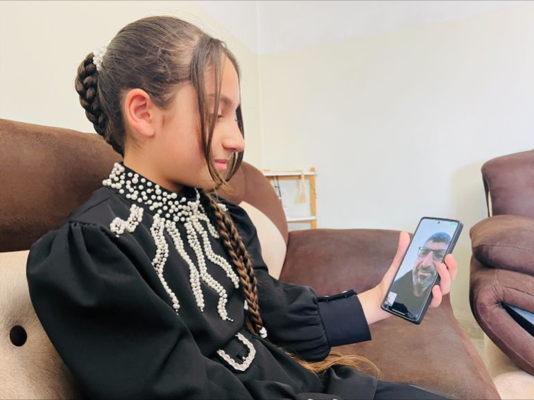 Bushra is holding her father's photo hoping to meet him soon [Fayha Shalash/Al Jazeera]