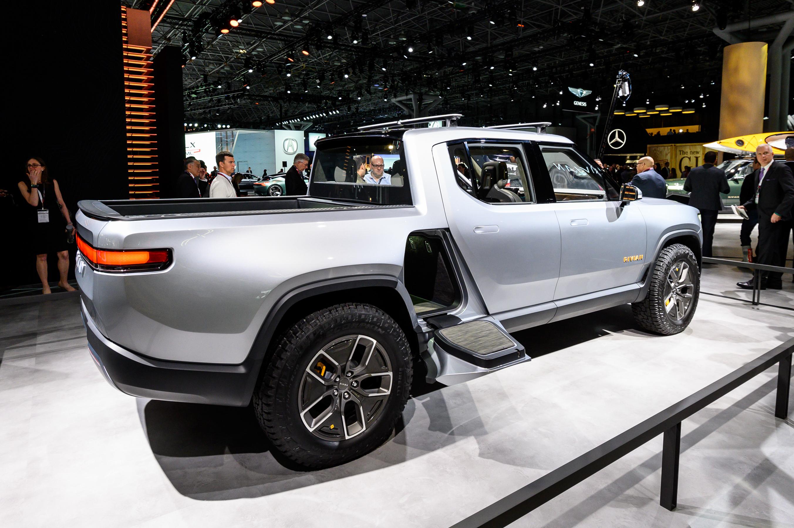 A silver Rivian R1T is on display with the door to the “Rivian Gear Tunnel” open.