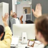 Cheerful aged woman, senior intern waving, saying goodbye to her young colleagues while leaving office after first day at work - stock photo