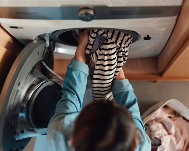 Overhead view of young Asian woman loading the washing machine with laundry - stock photo