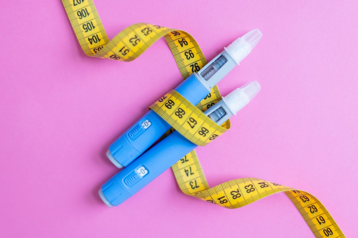 Two blue insulin pens wrapped with a yellow measuring tape on a pink background, symbolizing diabetes management, weight loss, medical treatment, and healthcare concepts. drugs injection ozempic - stock photo