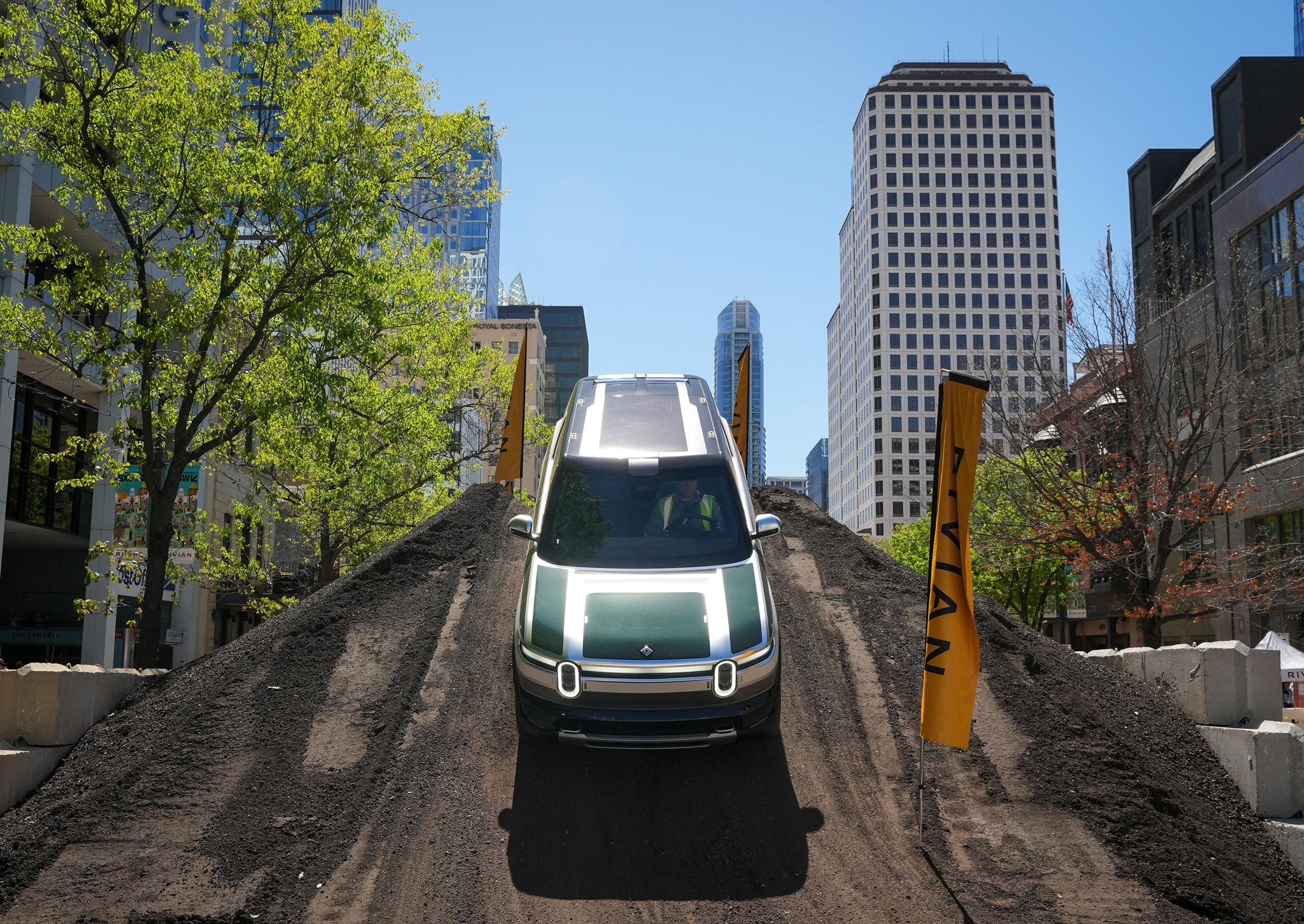 A Rivian R2 with a green hood is displayed on top of a large dirt mound in the city center as part of an activation for South by Southwest.
