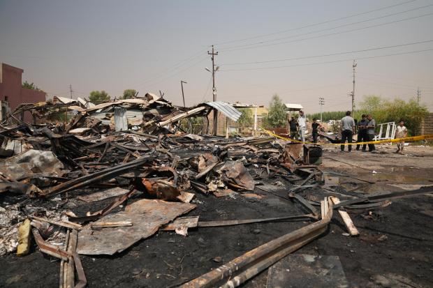 Iraqis inspect damaged structures at the site of an airstrike on a Popular Mobilization Forces base.