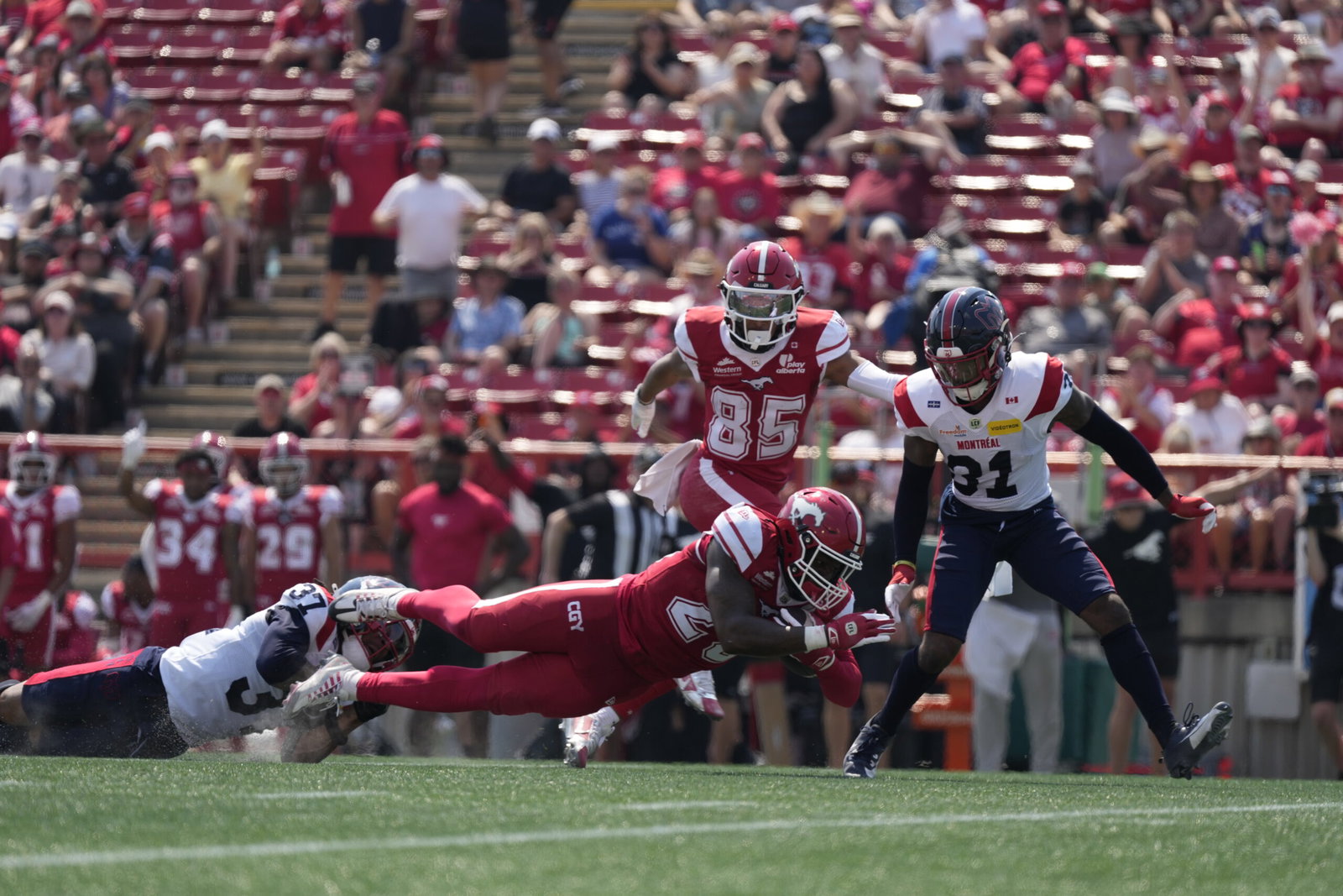 A football player in a red uniform dives toward the end zone as defenders attempt to tackle him during a game.