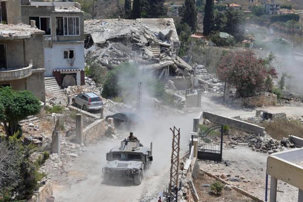A Lebanese military vehicle drives past homes damaged during the war.