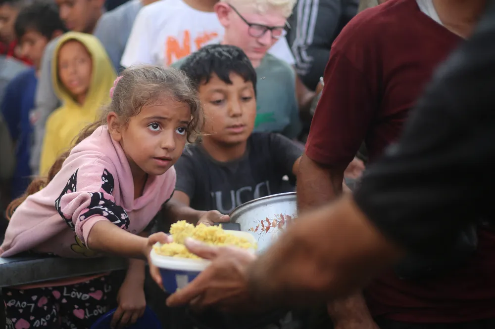A young child wearing pink reaches out to receive food from a person standing in front of them.