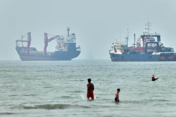 Children wade in the Strait of Hormuz with ships at anchor.