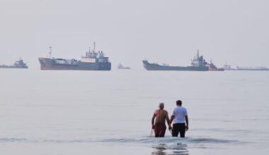 Two men wade in the waters of the Strait of Hormuz with vessels anchored in the background, off Bandar Abbas, Iran, on July 12.