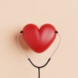 red heart shape with a stethoscope on a beige background, could illustrate concepts around healthy heart, cardiovascular health and heart disease