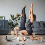 Young couple at home practicing yoga. They are watching online fitness live streaming classes.