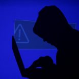 FILE PHOTO: A hooded man holds a laptop computer as blue screen with an exclamation mark is projected on him in this illustration picture taken on May 13, 2017. Capitalizing on spying tools believed to have been developed by the U.S. National Security Agency, hackers staged a cyber assault with a self-spreading malware that has infected tens of thousands of computers in nearly 100 countries. REUTERS/Kacper Pempel/Illustration/File Photo