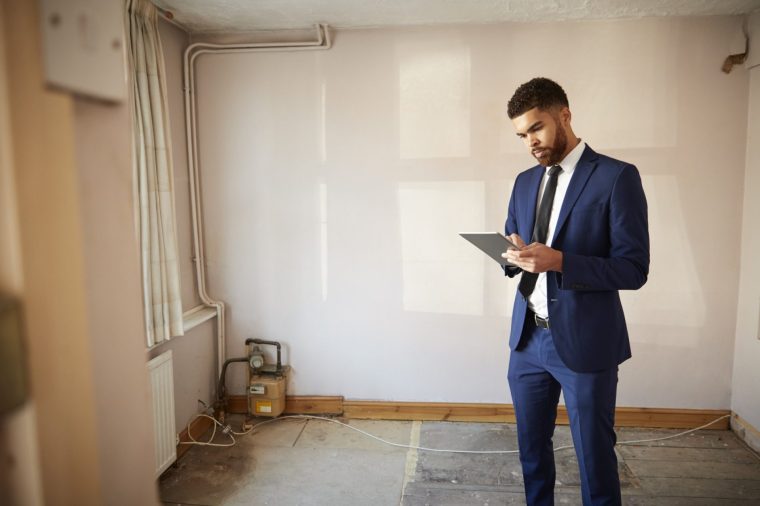 Male Real Estate Agent With Digital Tablet Carrying Out Valuation On Property For Renovation