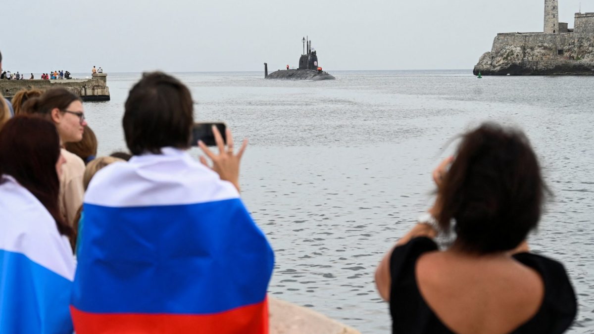 People with Russian flags look at the Russian nuclear-powered submarine Kazan, part of the Russian naval detachment visiting Cuba, arriving at Havana's harbour, June 12, 2024. The Russian nuclear-powered submarine Kazan -- which will not be carrying nuclear weapons -- and three other Russian naval vessels, will dock in the Cuban capital from June 12-17. The unusual deployment of the Russian military so close to the United States -- particularly the powerful submarine -- comes amid major tensions over the war in Ukraine, where the Western-backed government is fighting a Russian invasion. (Photo by YAMIL LAGE / AFP) (Photo by YAMIL LAGE/AFP via Getty Images)