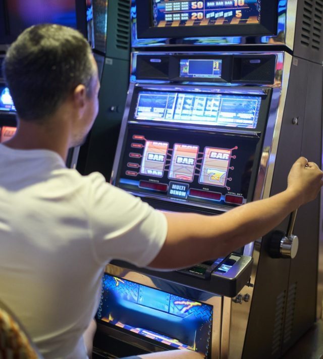 Man is sitting at a slot machine while focusing on the game. Scene is illustrating gambling, entertainment, and casino atmosphere.