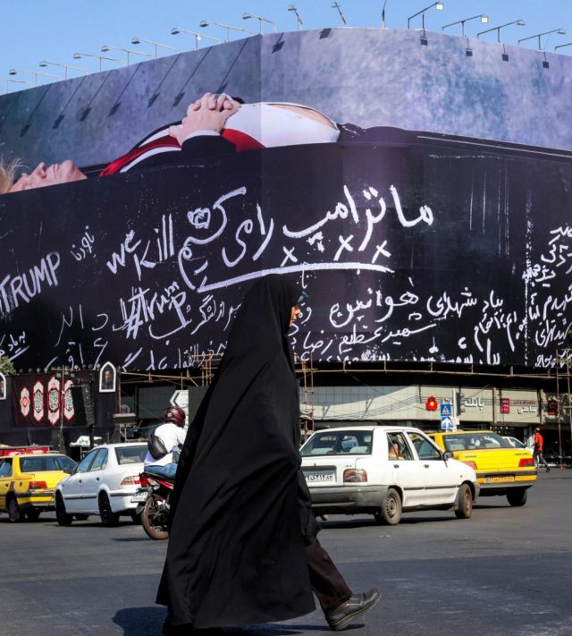 TOPSHOT - A woman crosses Tehran's Enghelab Square on July 15, 2026, past a giant anti-US billboard featuring US president Donald Trump in a coffin with text in Persian reading "We Kill Trump". Hostilities renewed between Iran and the US, endangering a memorandum of understanding, reached in June with Qatari and Pakistani mediation, aimed at ending the war. The confrontation resumed on July 7 after attacks on ships in the Gulf, which Iran has attributed to Iran. (Photo by AFP via Getty Images) /