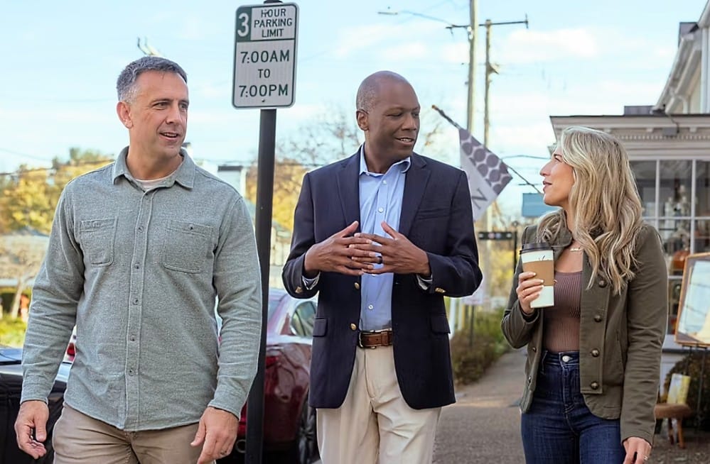 Three casually dressed adults walk and chat along a sunny street; a sign behind them shows 3-hour parking 7:00 AM–7:00 PM.