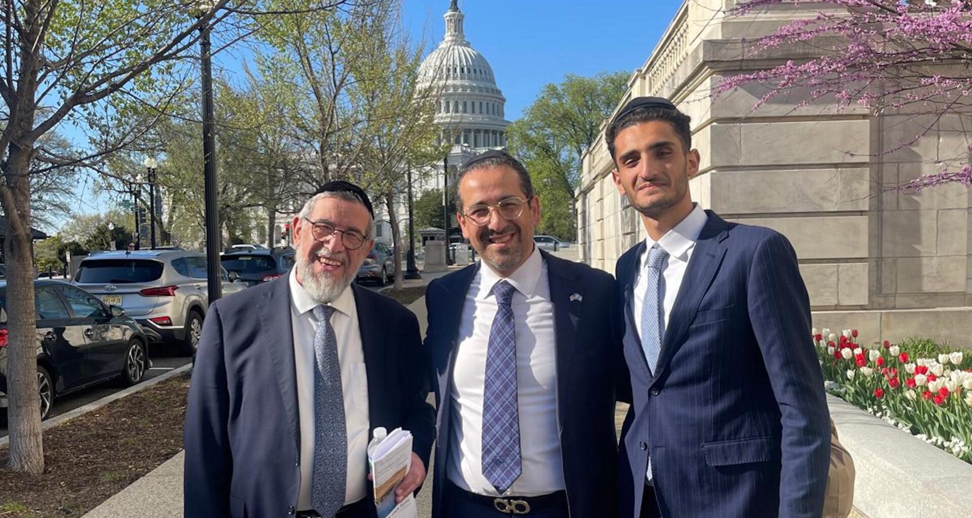 A photo of three men posing in from of the capitol building.