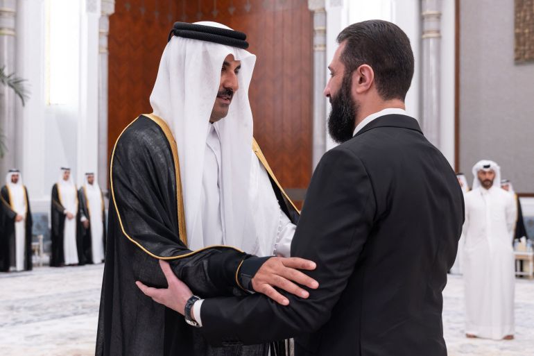 This handout photograph taken and released by Qatar's Amiri Diwan on July 13, 2026 shows Qatar's Emir Sheikh Tamim bin Hamad Al Thani (L) receiving condolences from Syria's President Ahmed al-Sharaa, following the death of his father, former leader Sheikh Hamad bin Khalifa Al Thani, at the Lusail Palace on the outskirts of Doha.