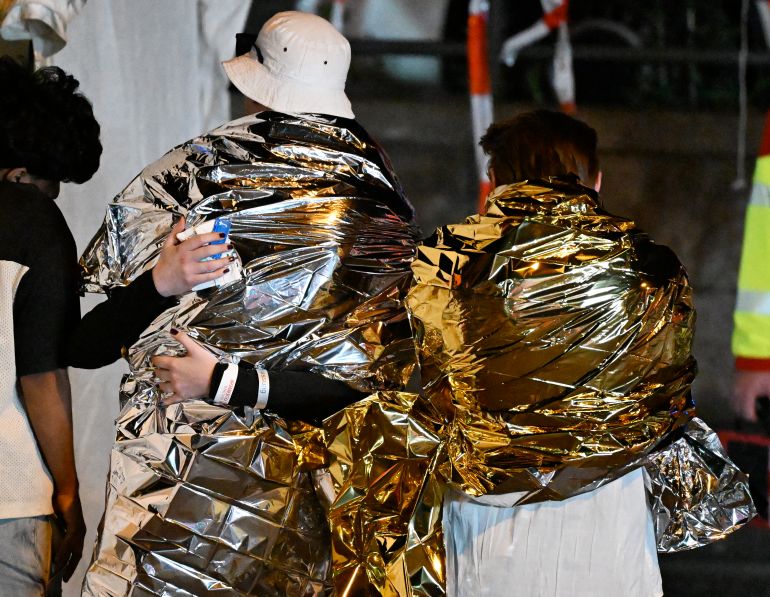 People wrapped in security blankets hug near the scene where one person was killed and around 15 injured after a car is believed to have hit the crowd on the outskirts of the Christopher Street Day (CSD) parade in Berlin, on July 25, 2026.