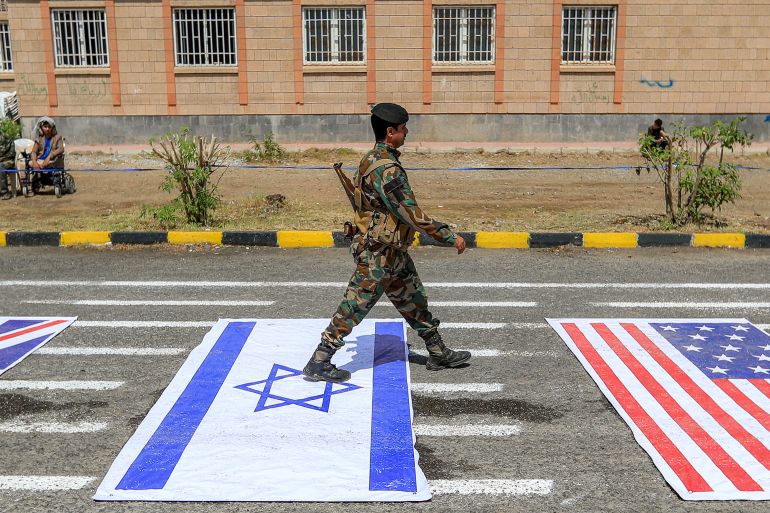 A fighter loyal to Yemen's Houthi movement walks over depictions of the Israeli and US during a demonstration by university students to show their support for the Houthis amid escalating tensions with Saudi Arabia, at the Sanaa University campus in the Houthi-held capital Sanaa on July 22, 2026.