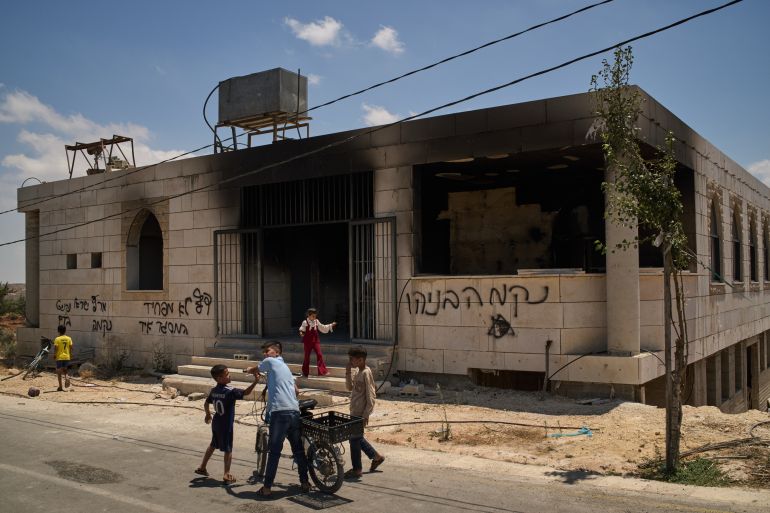 Children stand outside a mosque that was burned during an attack by Israeli settlers early in the morning in the West Bank village of Qusra, Sunday, July 26, 2026, as on its wall a Hebrew graffiti reads "Revenge Benayahu", referring to an Israeli settler killed during clashes with Palestinians in the village of Tell, last Friday. (AP Photo/Leo Correa)