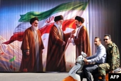 Men ride a scooter past a billboard featuring the images of the late founder of the Islamic Revolution, Supreme Leader Ayatollah Ruhollah Khomeini (left), his successor Ali Khamenei (center) and his son, the current Supreme Leader Mojtaba Khamenei.