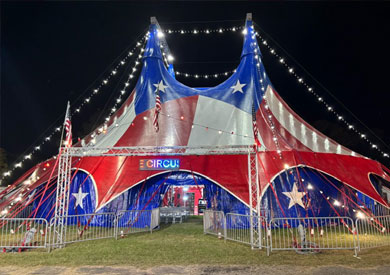 Circus tent decorated with red, white, and blue colors and stars, lit up at night.