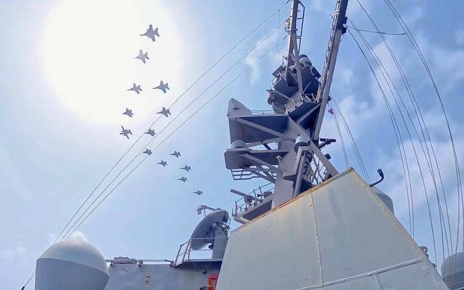 A formation of aircraft fly over a warship.