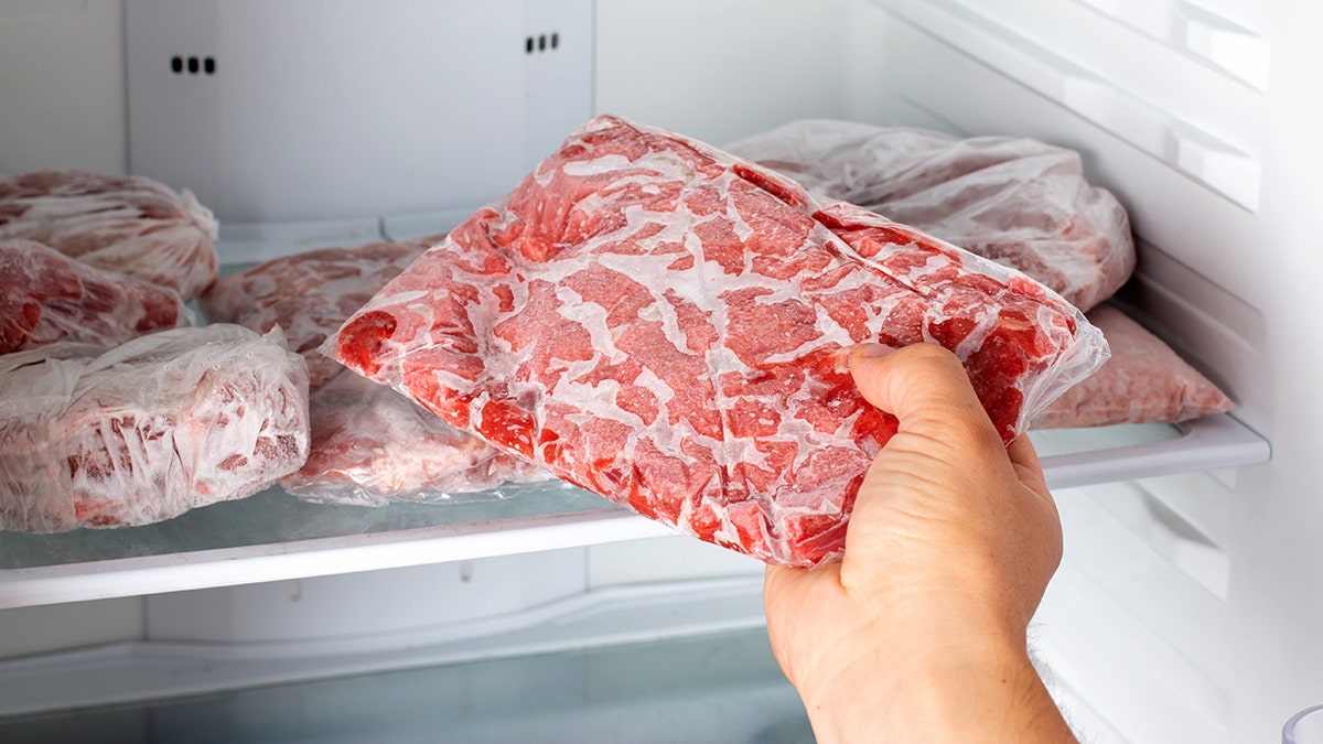 A hand picks up frozen meat from a freezer.