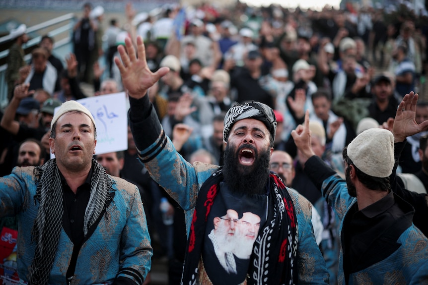A man with an Ali Khamenei T-Shirt shouts and raises his hand, at the front of a crowd of mourners in Tehran.