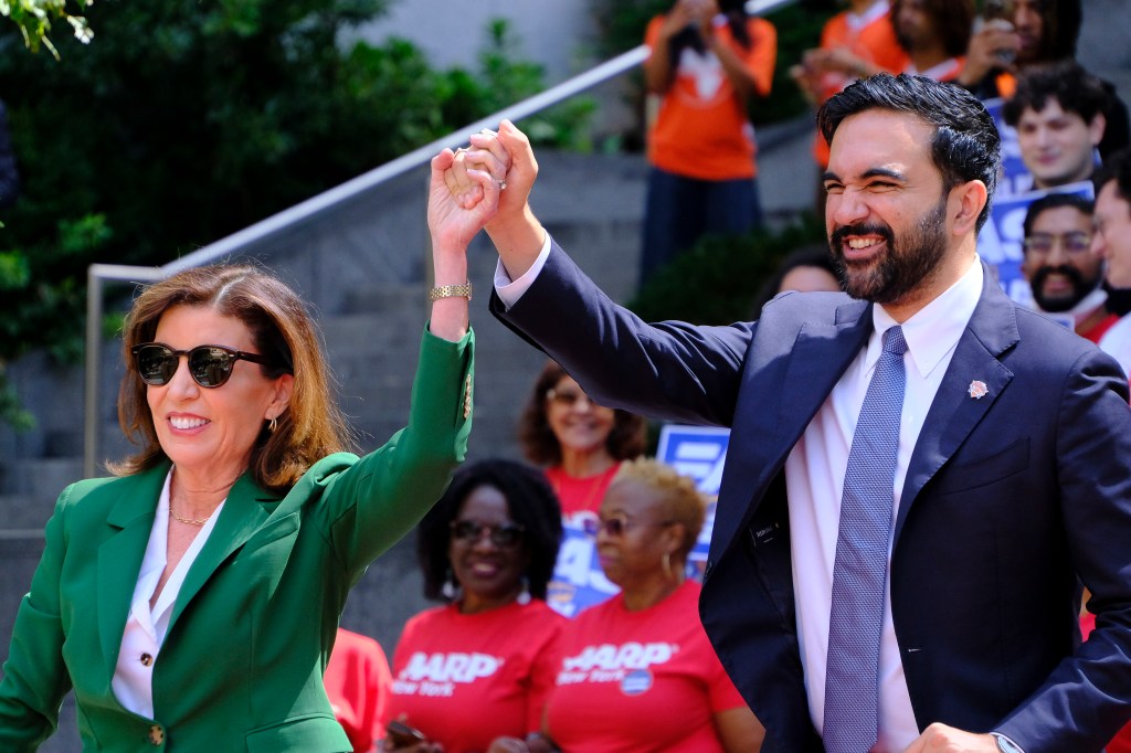New York Governor Kathy Hochul and Zohran Mamdani raising their clasped hands.