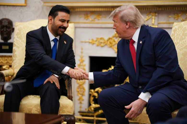 Two men in suits shakes hands while seated.