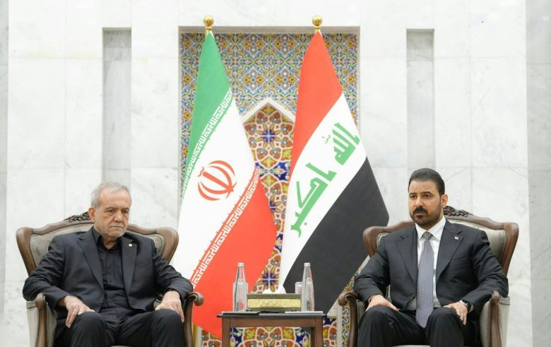 Two leaders in suits sit side by side flanked by national flags.