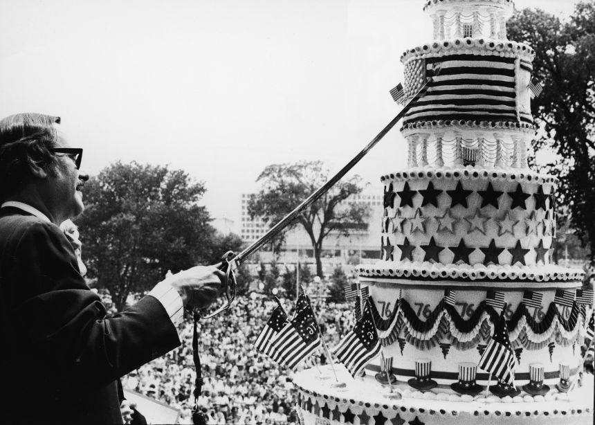 US archivist James B. Rhoads cuts a giant birthday cake at a bicentennial parade in DC.