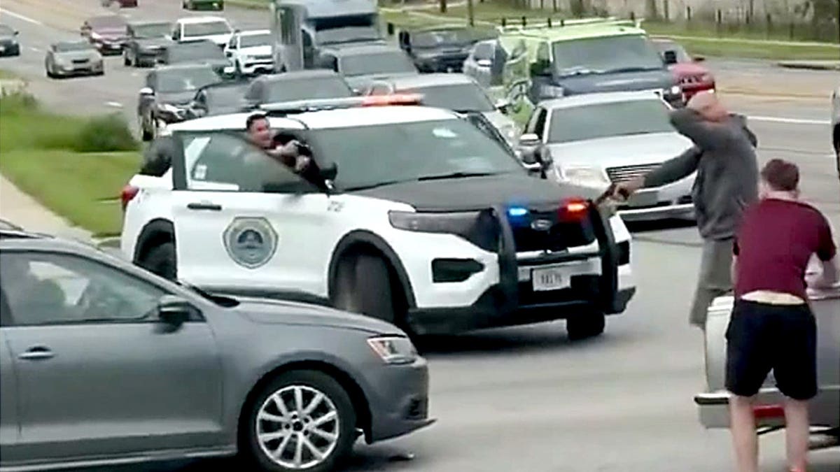 A man stands in the roadway pointing a handgun toward another vehicle following a crash.