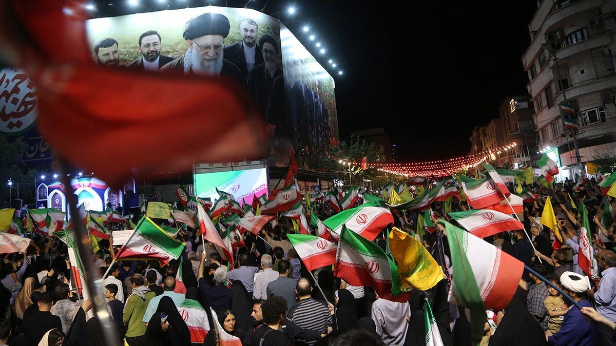 Thousands of people gather at Revolution Square in Tehran holding Iranian flags and posters.