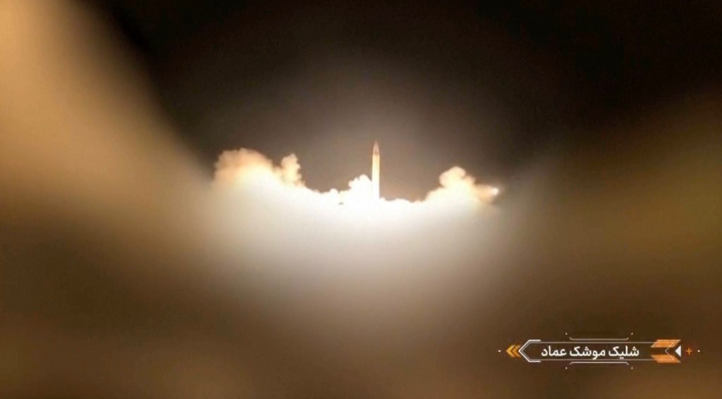 A missile launching from a dark landscape into a dark sky, surrounded by white smoke and bright light from the launch, with Farsi text in the bottom right corner.