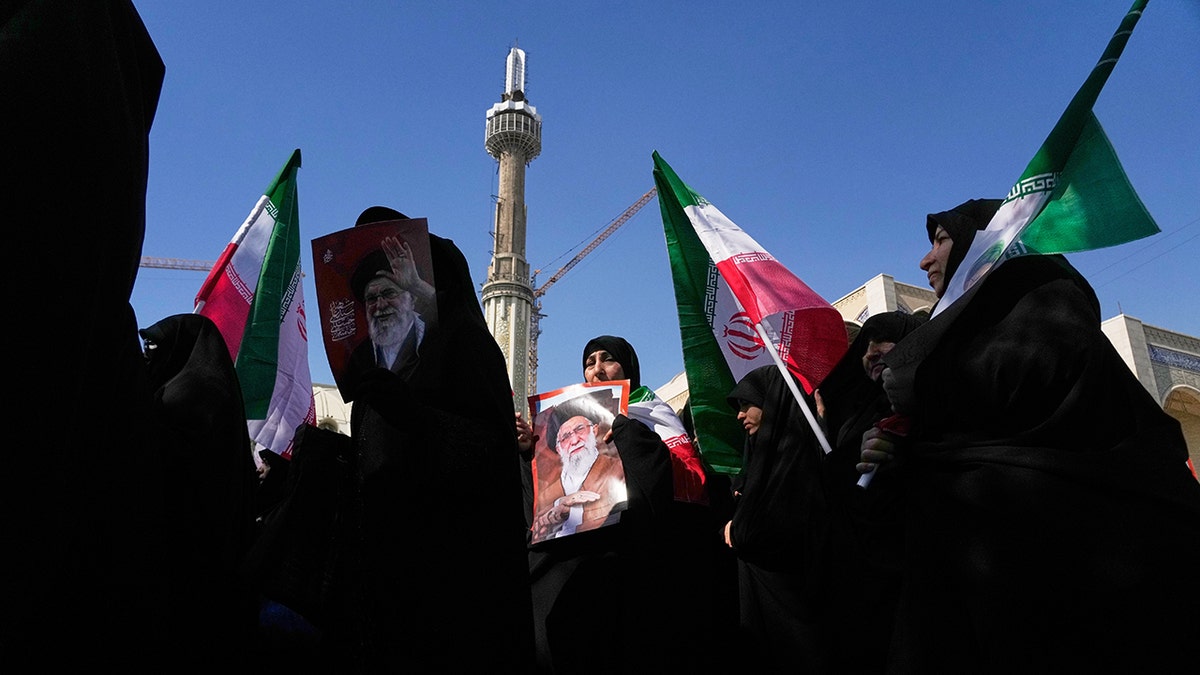 Women holding Iranian flags and portraits of the late Supreme Leader Ali Khamenei at a mosque.