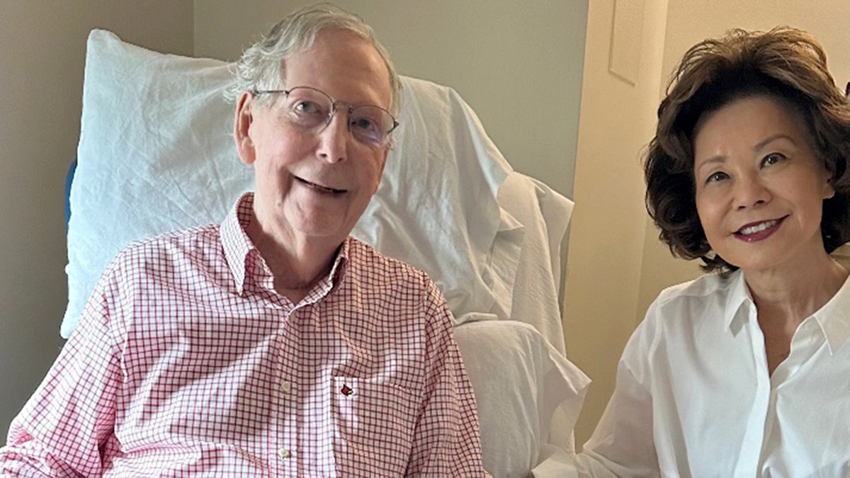 Mitch McConnell sits from a hospital chair next to his wife.