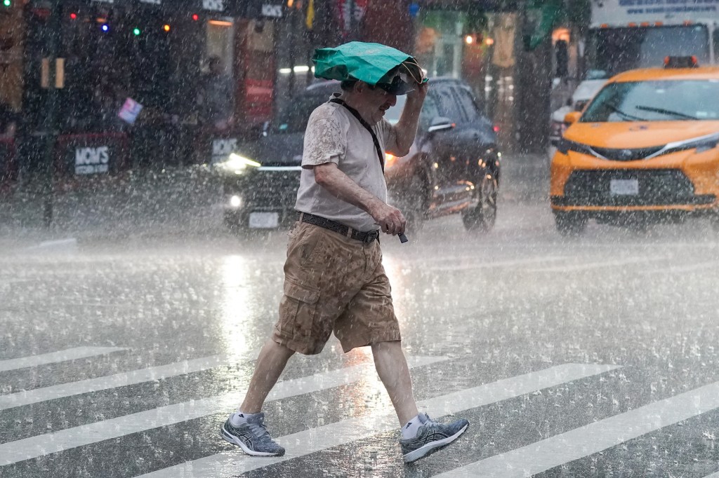 Man crossing a street in Hells Kitchen, NYC during a heavy rain shower, using a paper bag as an umbrella.
