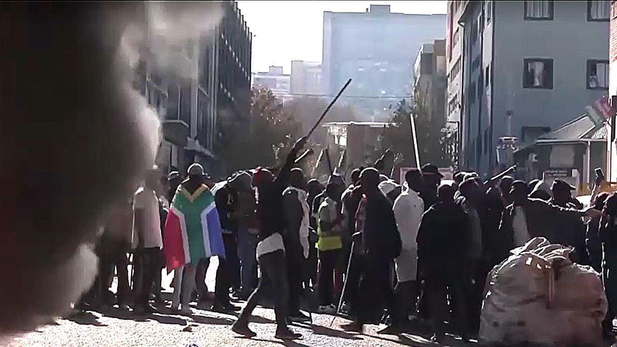 Protesters holding wooden sticks near a fire in a Johannesburg street