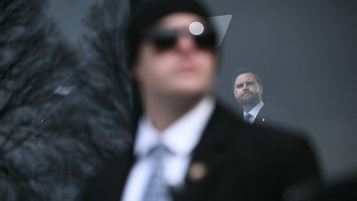 Secret Service agent watches crowd as Vice President JD Vance speaks behind bulletproof glass.