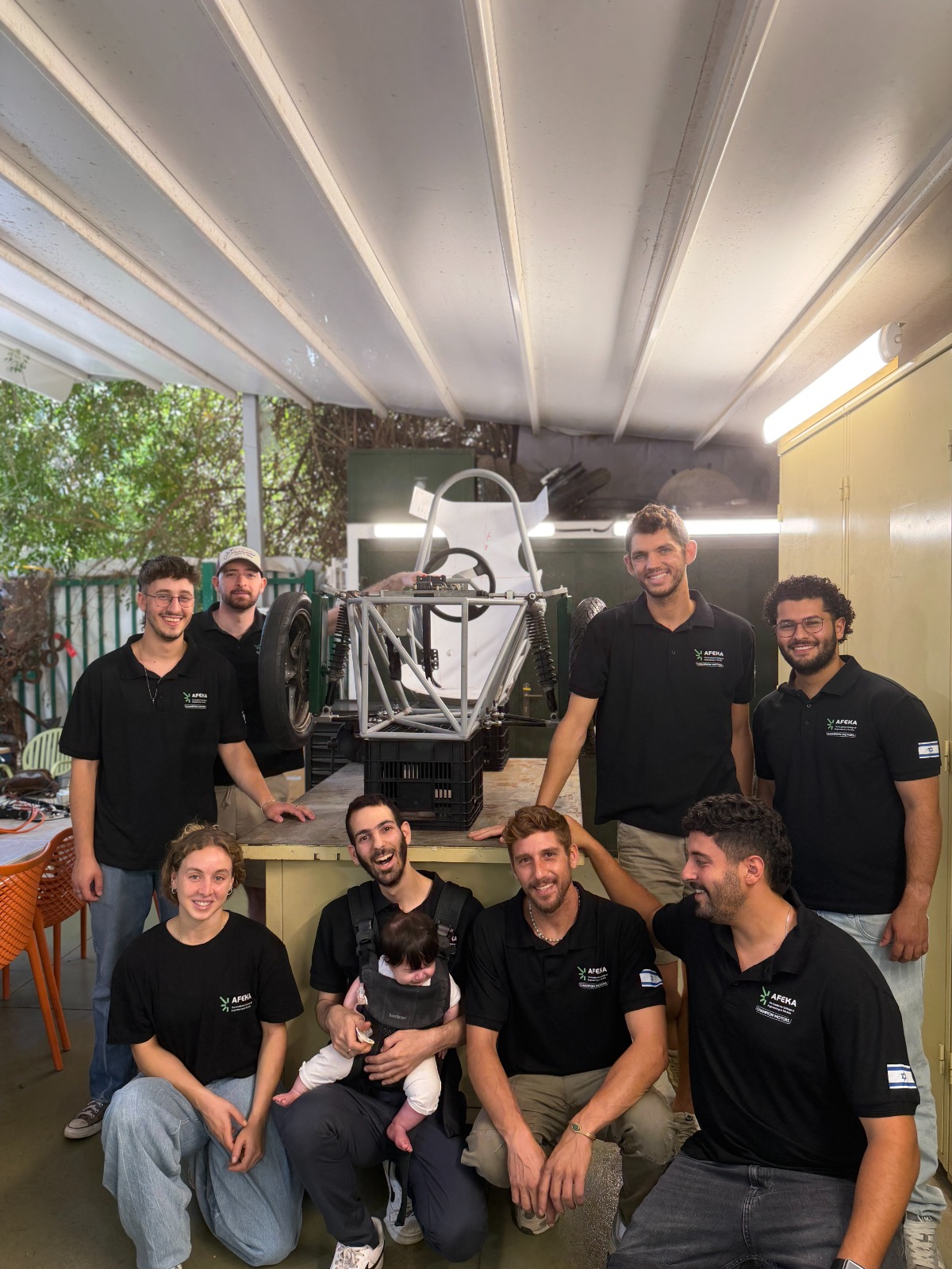 Some of the team members (and extended family members) of Afeka Racing who are building a solar vehicle (in the background), July 2026. Credit: Afeka Auto Club.