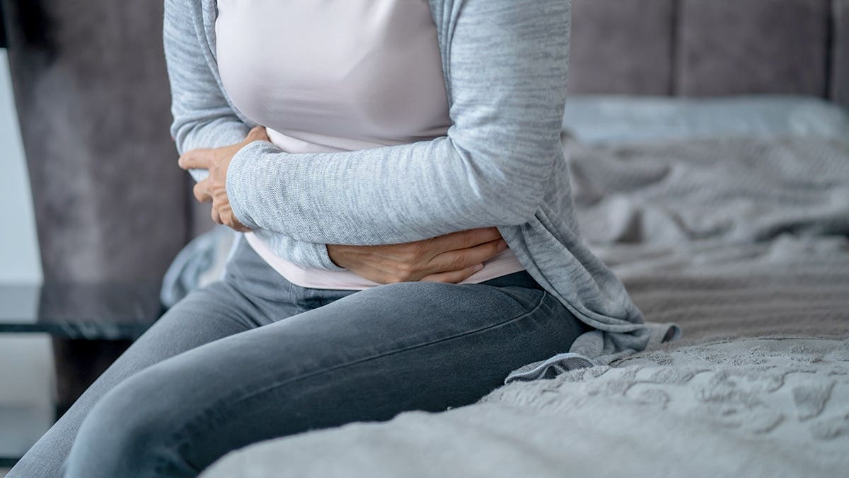 Woman feeling stomach ache and holding belly in hands sitting on bed